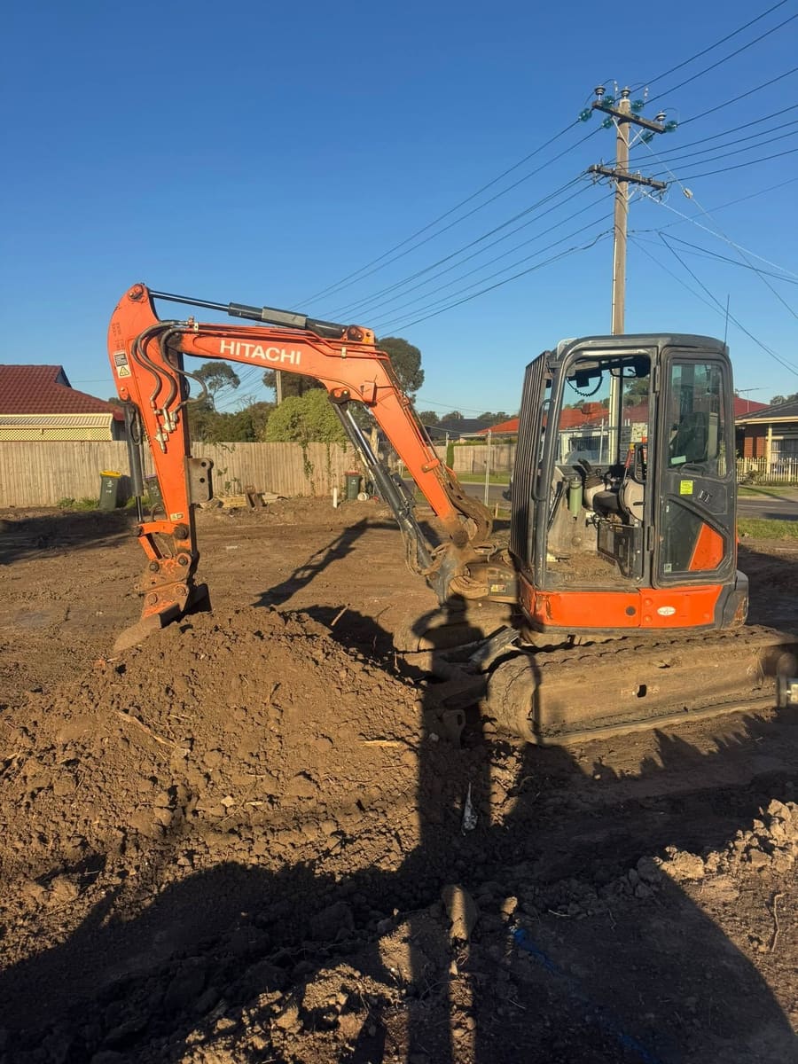 An excavator parked on a freshly graded block in late afternoon light, with the ground worked flat around it.