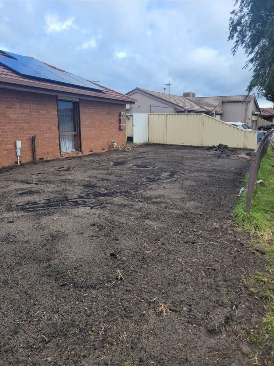 After: the same side yard cleared to bare, graded soil running clean from the house wall to the fence.